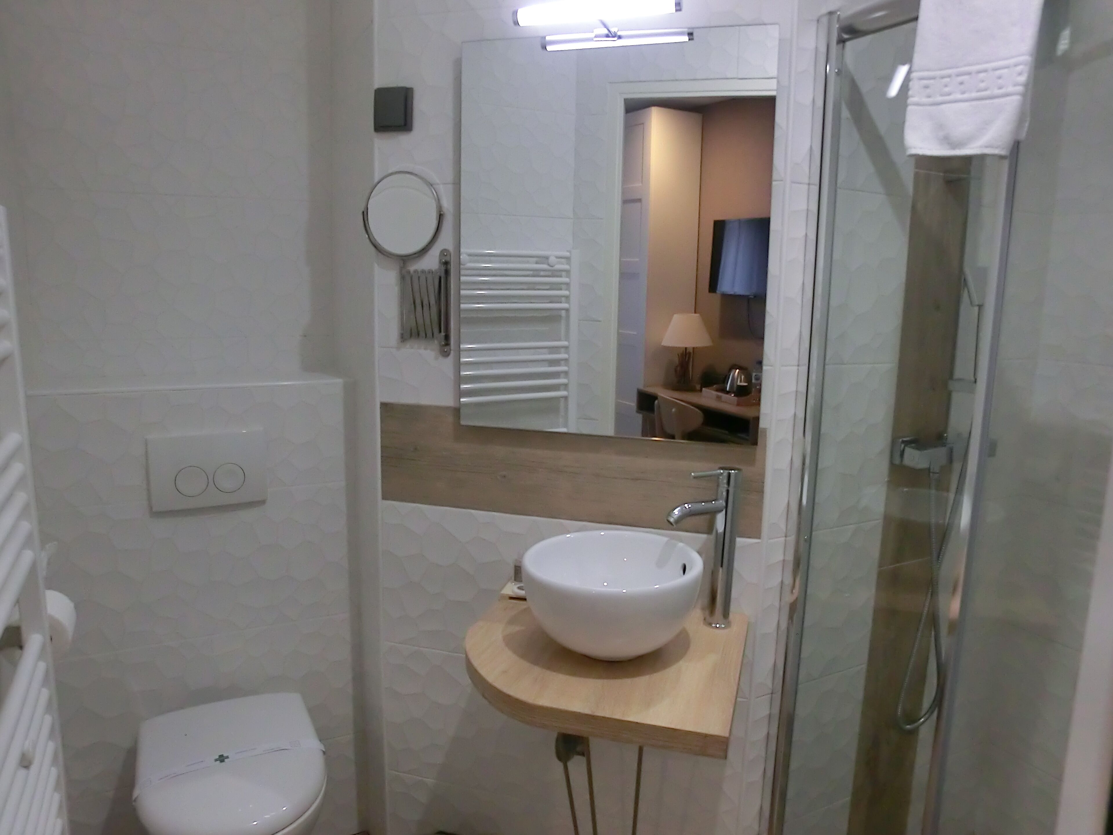 A modern bathroom with a white toilet, a wooden vanity with a white sink, a mirror, and a glass shower enclosure.