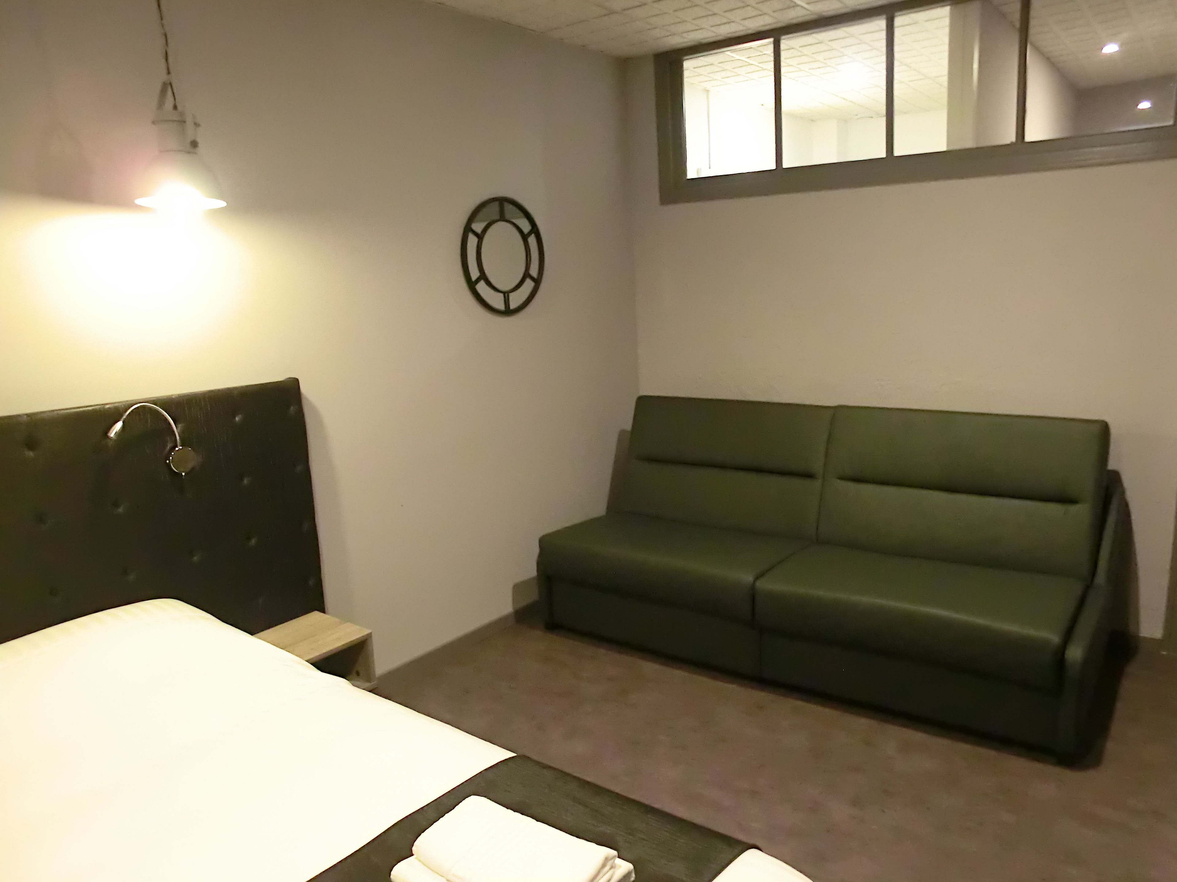 A room with a bed, a green sofa, a wall clock, and a window.