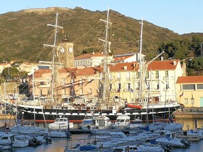 A harbor with several boats docked, a prominent tall ship with masts, and buildings with red-tiled roofs in the background. - Hôtel sur le Quai (Port-Vendres)