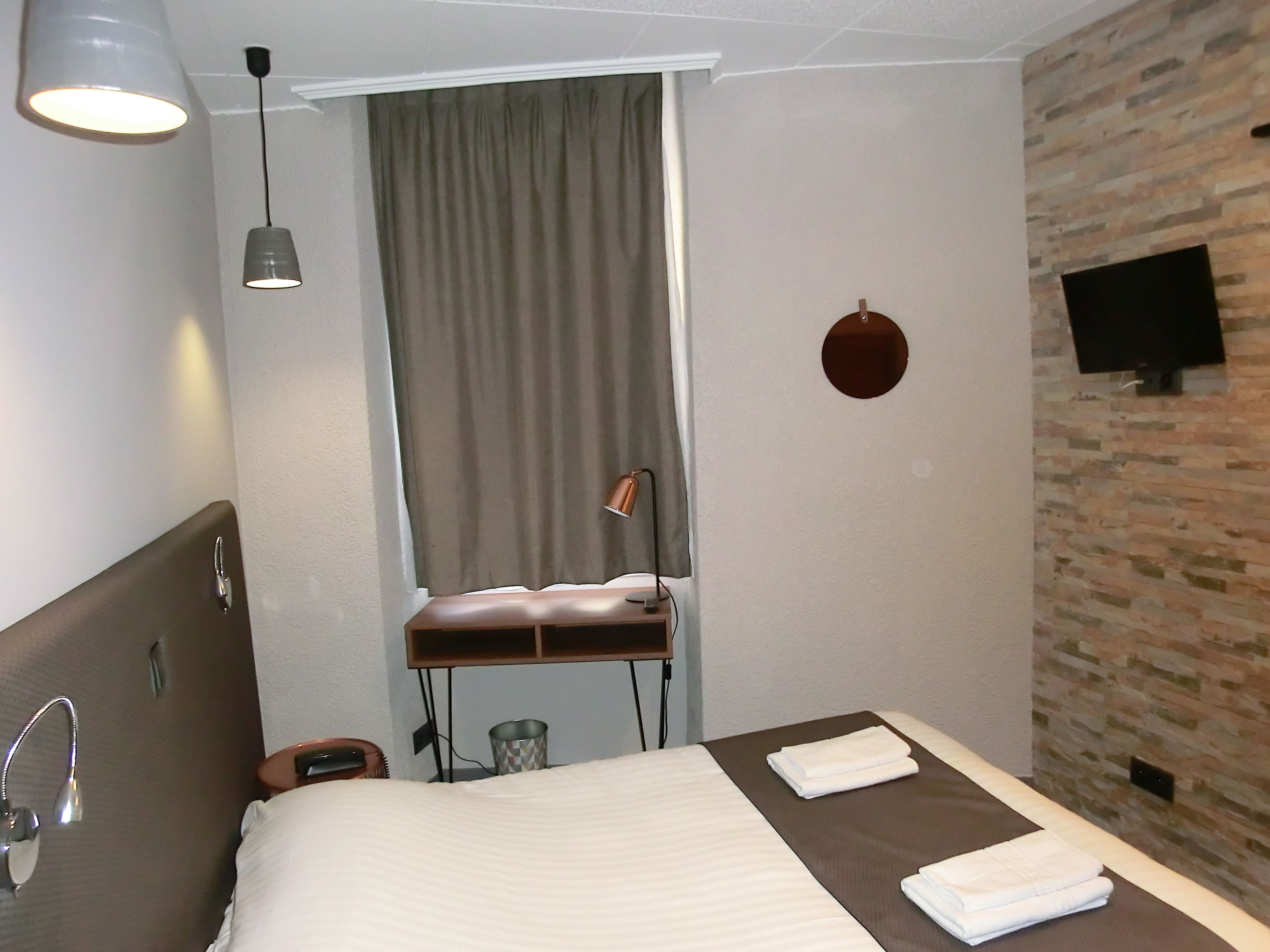 Habitación de hotel con cama, escritorio, silla, televisor en la pared y ventana con cortinas.