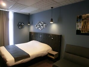 Un dormitorio moderno con una cama grande, una mesita de noche pequeña, un cabecero con un cuadro de un pez decorativo, y una pintura en la pared.