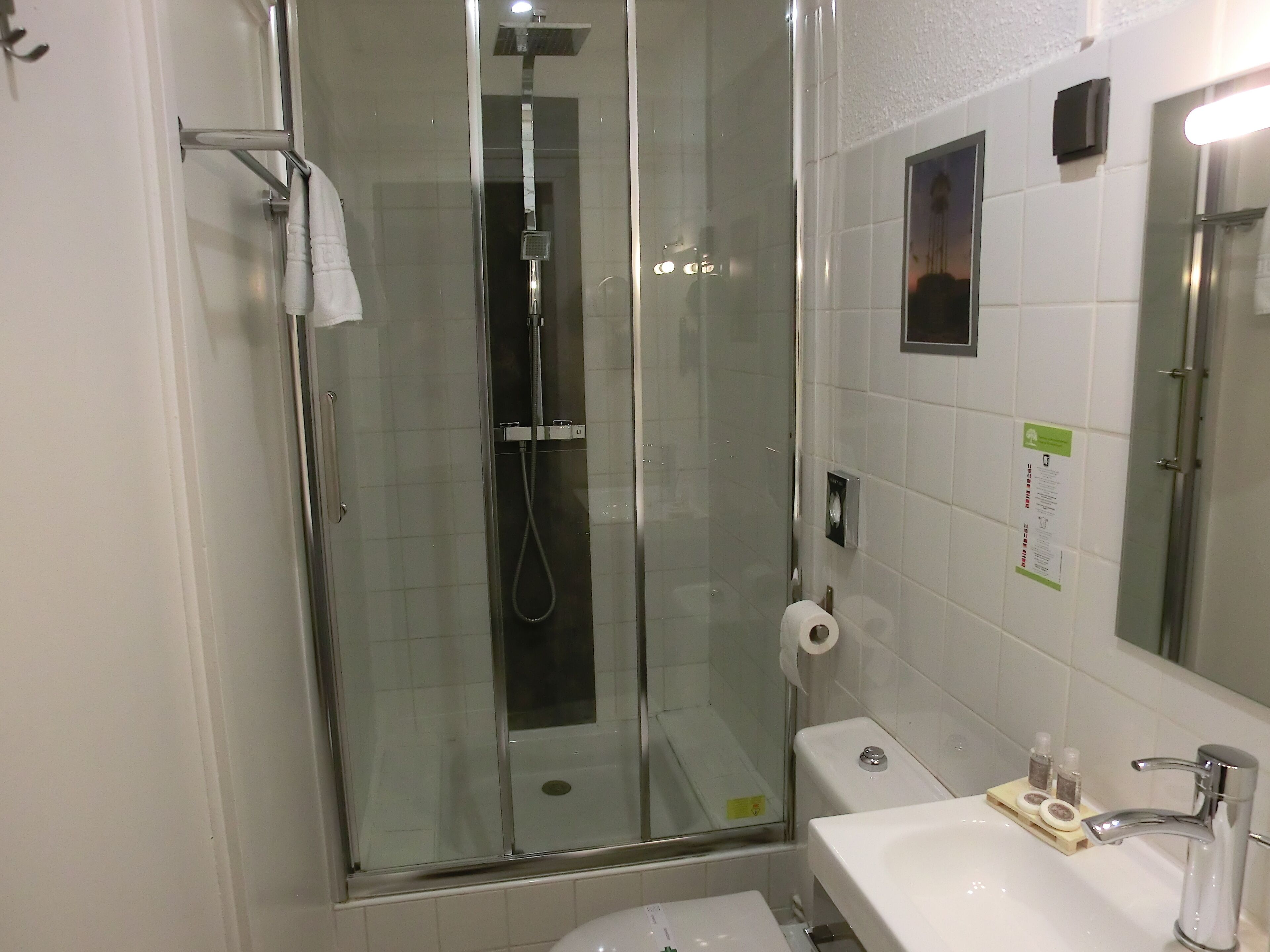 A glass-enclosed shower with a handheld showerhead, a toilet, and a sink with soap dispensers.