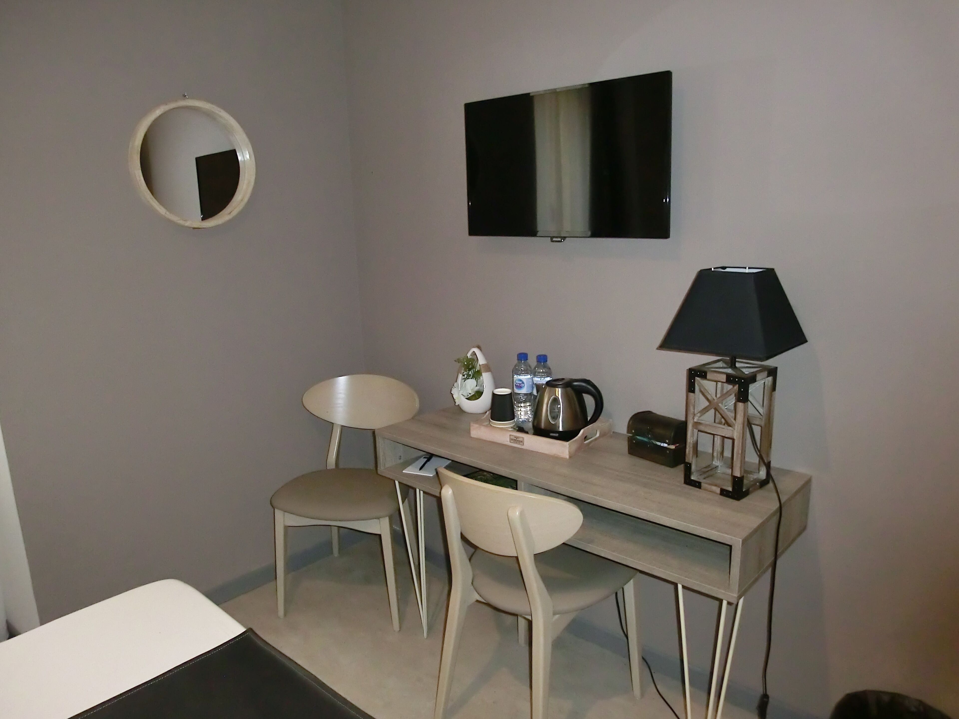 A small, modern room with a desk, two chairs, a television, a lamp, and a mirror.