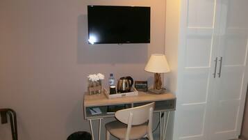 A hotel room with a desk, chair, television, lamp, and a wardrobe.