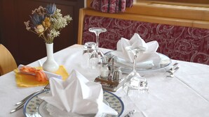 Ein Tisch ist mit einer weißen Tischdecke, blau-weißen Tellern, Besteck und einer Vase mit getrockneten Blumen gedeckt.
