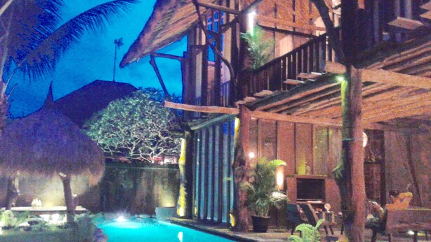A pool area with a thatched-roof structure, a wooden deck, and surrounding greenery. - Rustic Hut in Seminyak Bali (Seminyak)