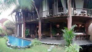 A wooden house with a pool, outdoor seating, and a thatched roof. - Rustic Hut in Seminyak Bali (Seminyak)