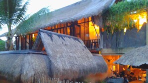 A thatched-roof building with a balcony, a wooden fence, and a small garden area. - Rustic Hut in Seminyak Bali (Seminyak)