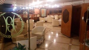 A lobby with a checkered floor, white armchairs, a glass partition with a decorative design, and a framed artwork on the wall. - Spor Hotel (Ankara)