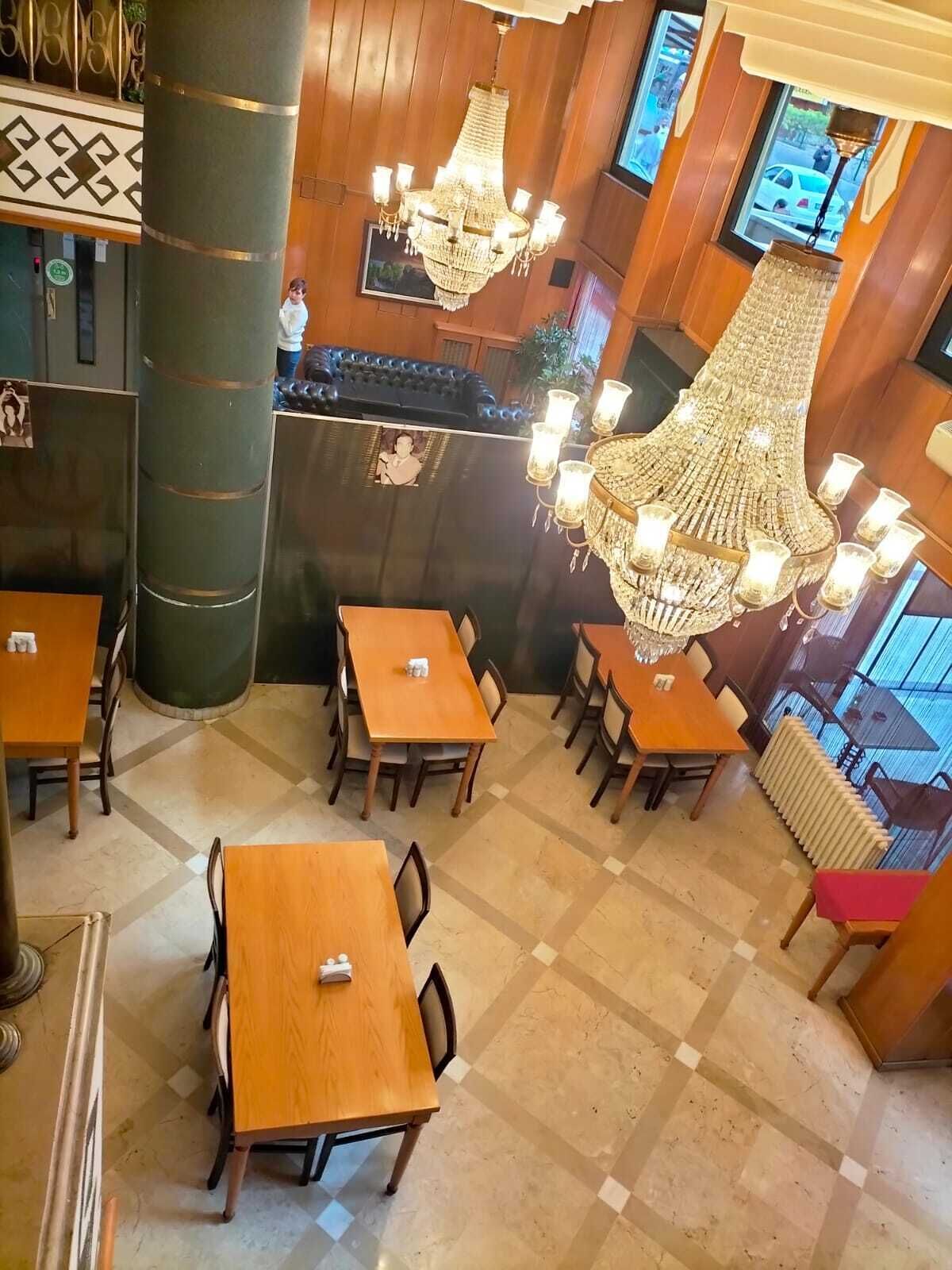 A restaurant with wooden paneling, multiple chandeliers, and several tables and chairs.