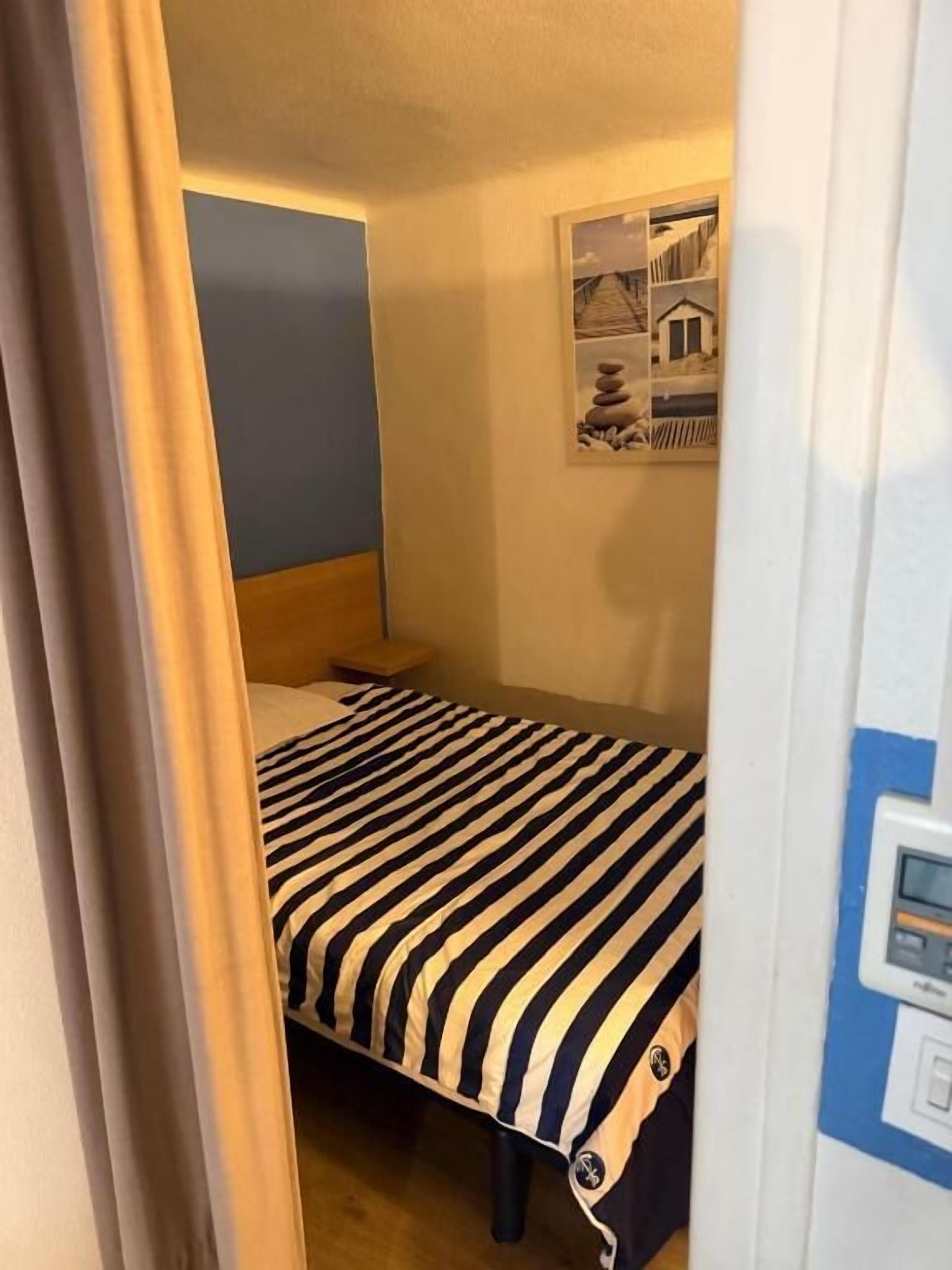 A small room with a bed, a nightstand, a wall-mounted picture, and a door.