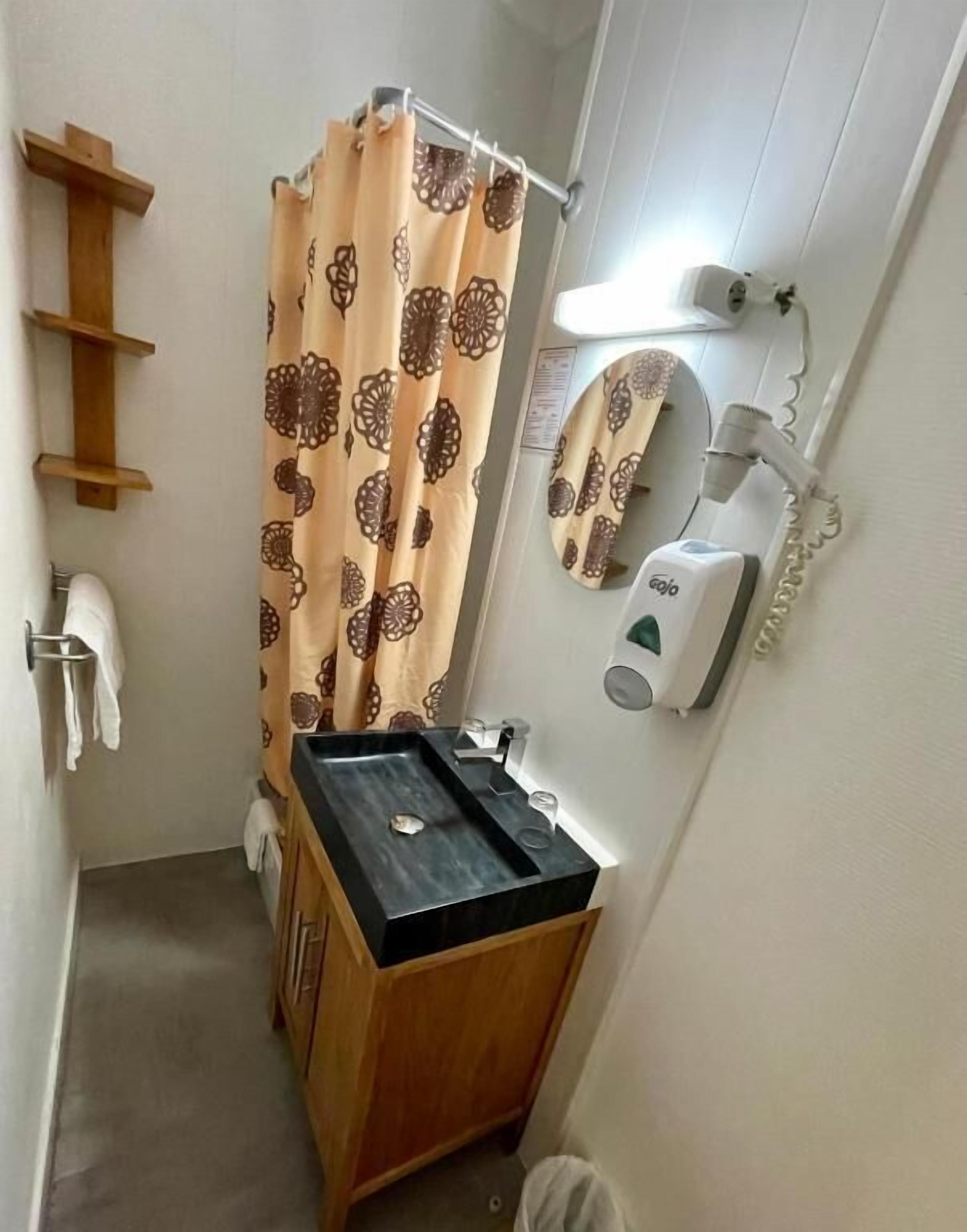 A small bathroom with a wooden vanity, a shower curtain, a hand dryer, and a wall-mounted mirror.