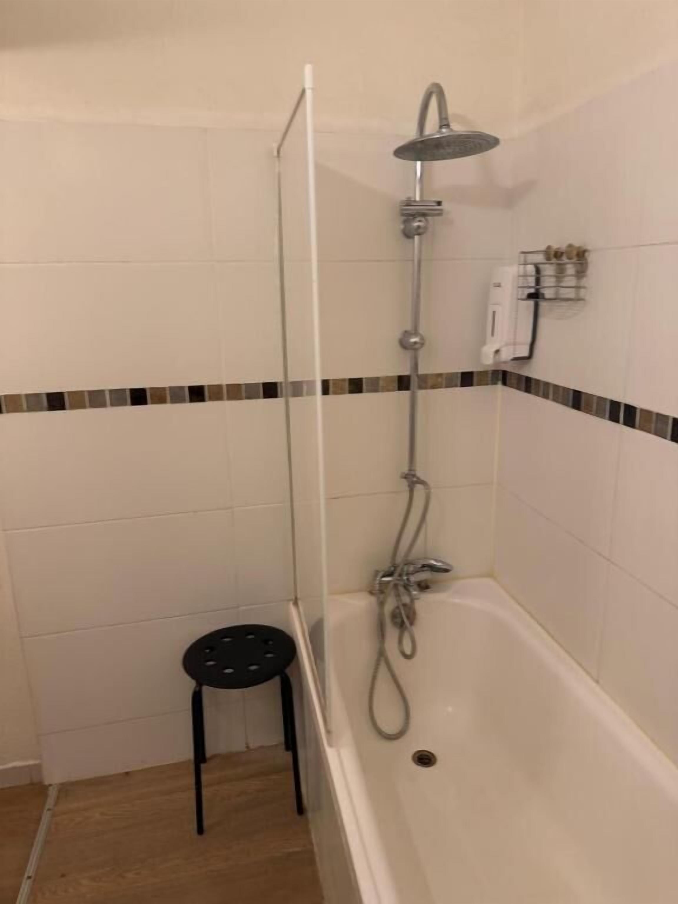 Un baño con ducha, bañera y un taburete pequeño.