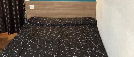 A bed with a geometric patterned bedspread, a teal wall with a light fixture, and three teal wall hangings.