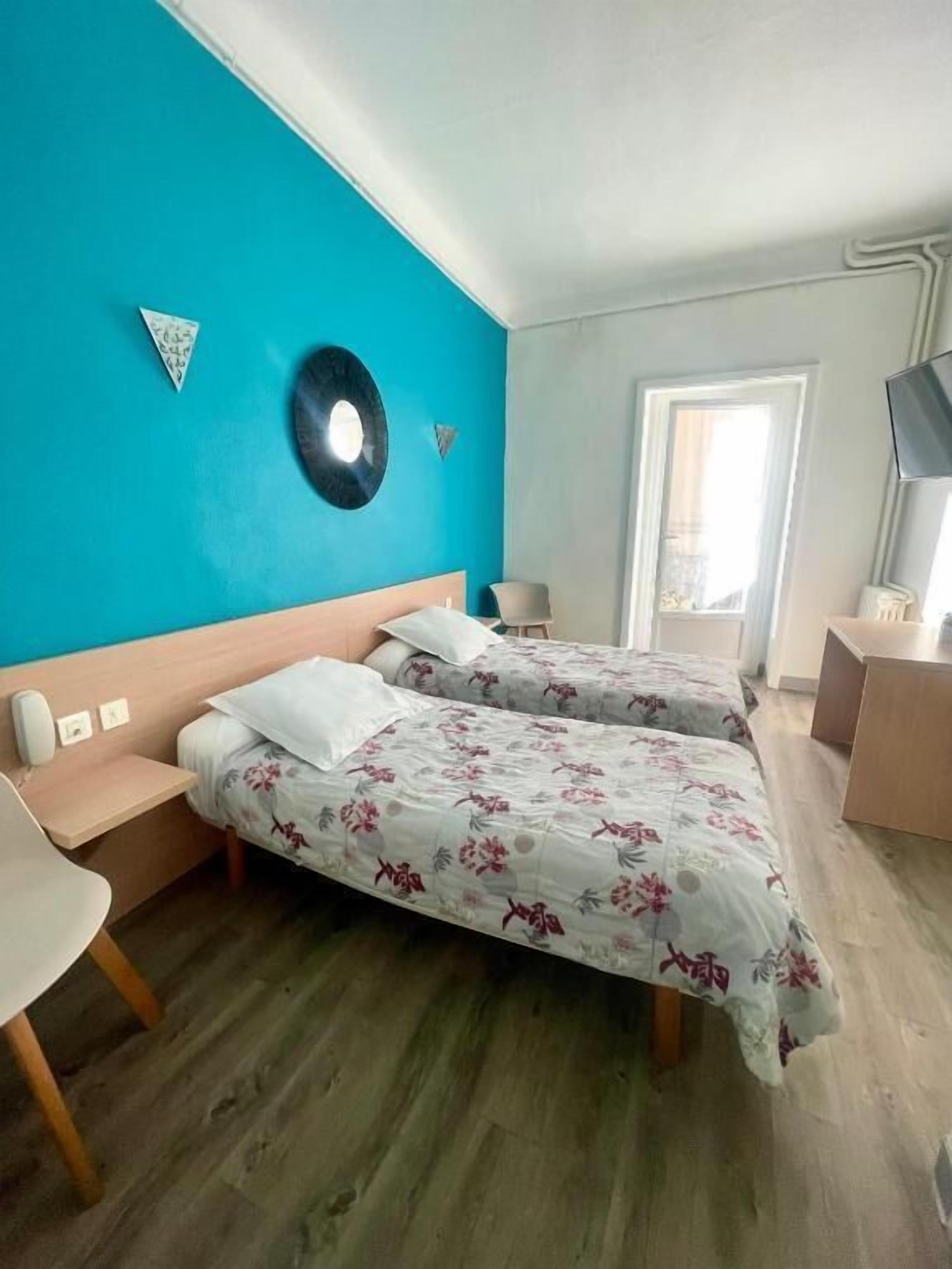 A room with two beds, a desk, a chair, a television, and a window.
