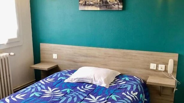 Une chambre à coucher comprenant un lit, une table de chevet, un tableau accroché au mur et deux appliques murales.