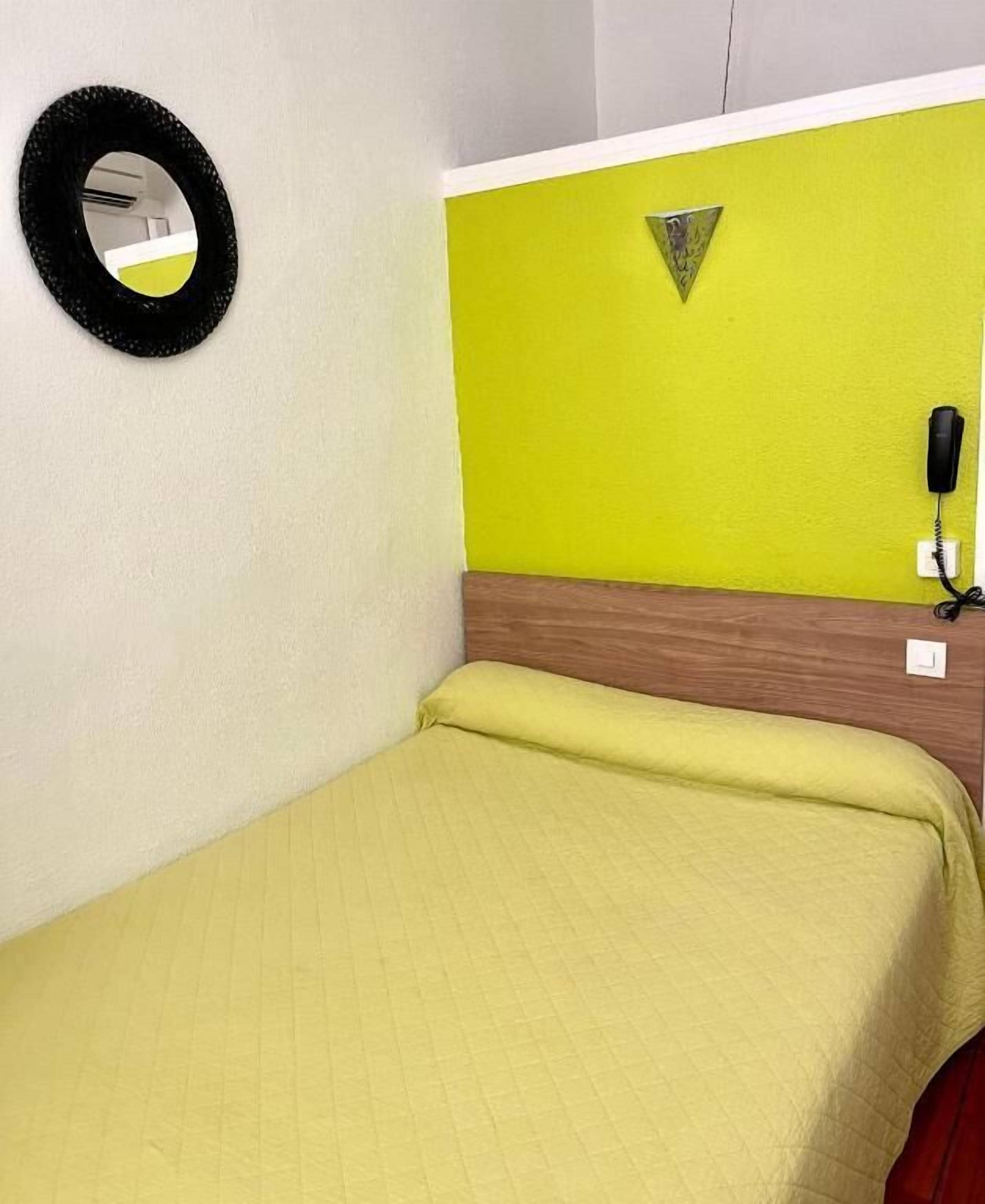 A small room with a bed, a mirror, a phone, and a wall with a triangular decoration.