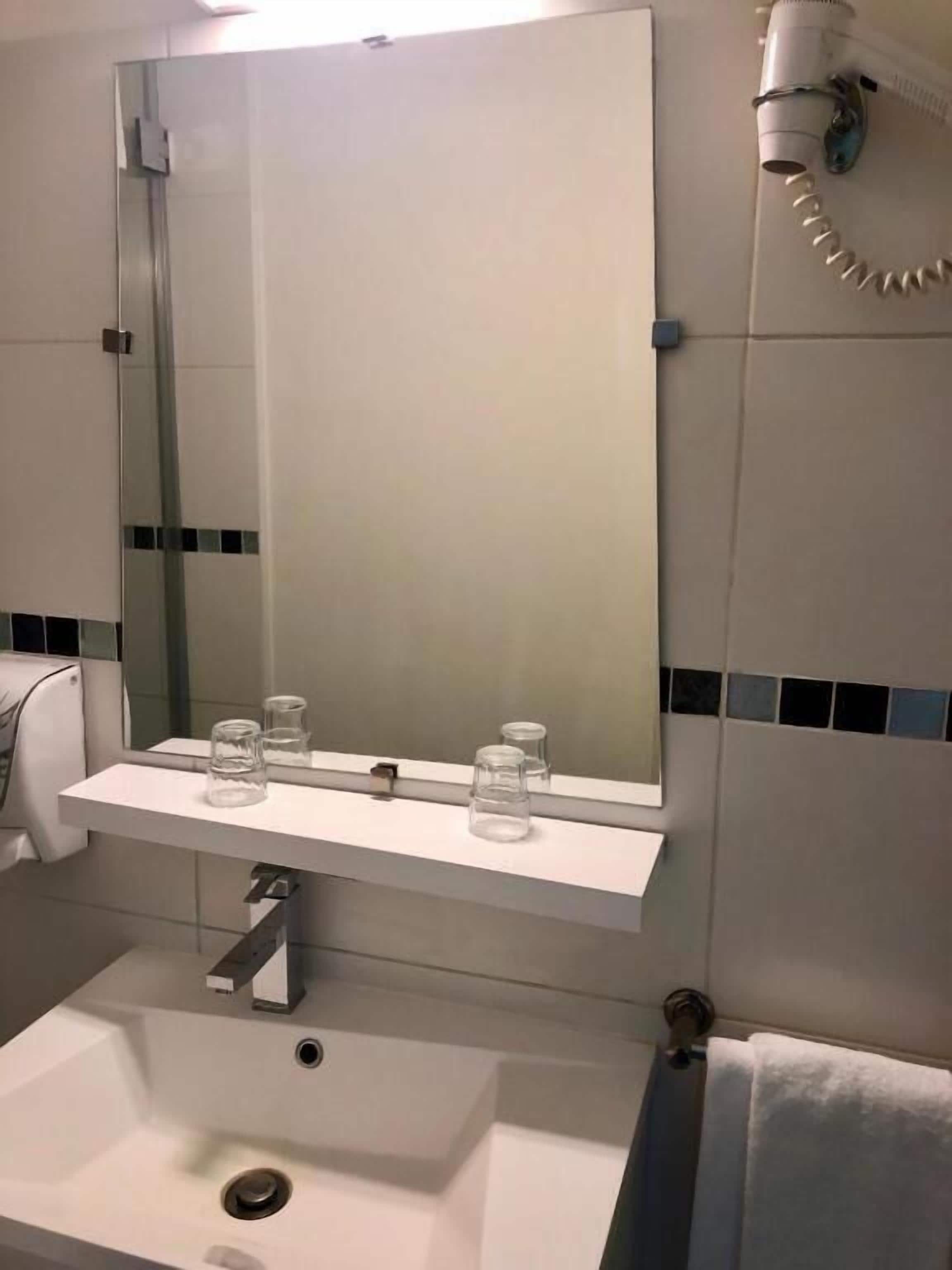 Un bany amb un lavabo blanc, un mirall i un penjador de tovalloles.