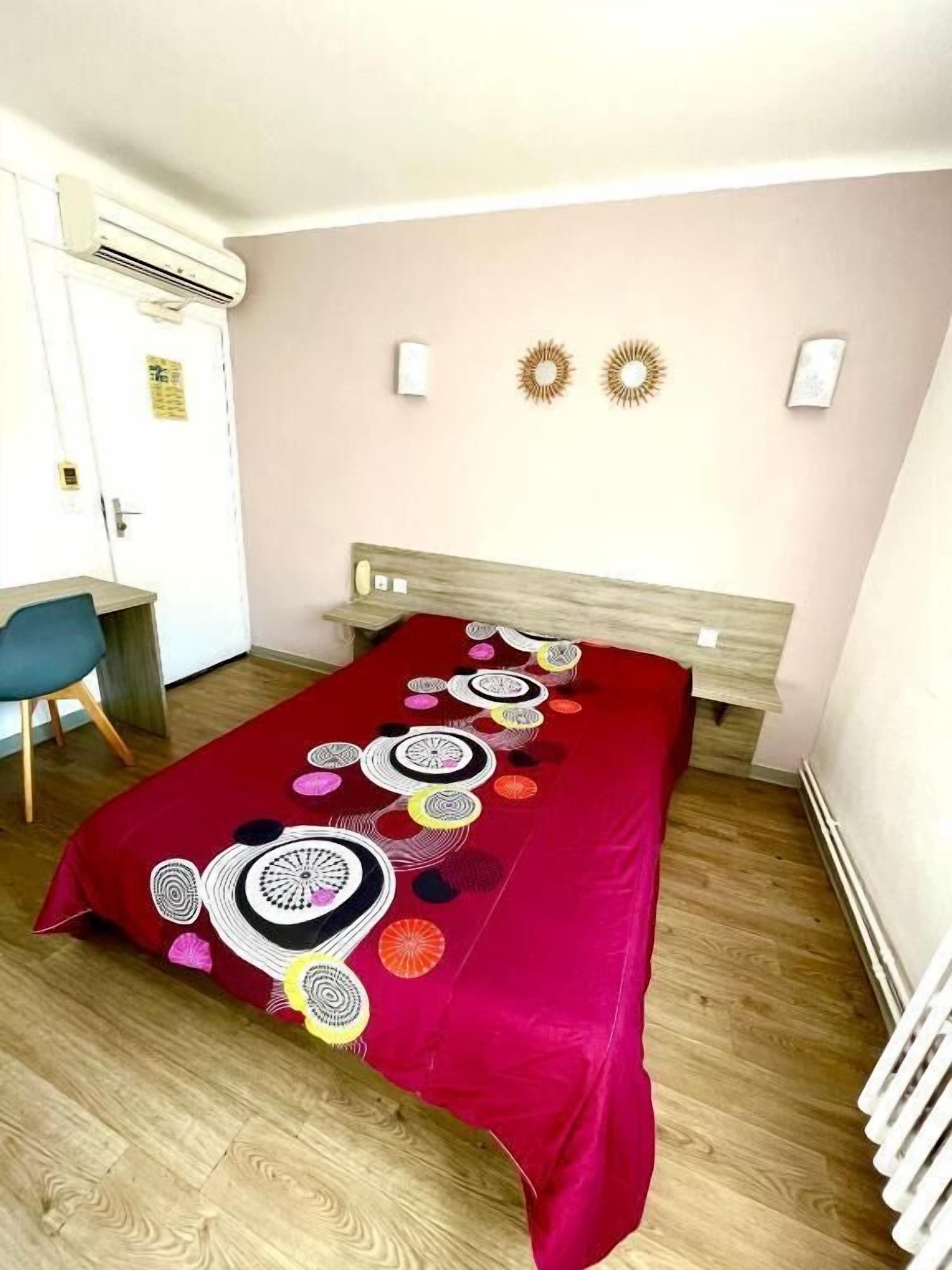 Une pièce comprenant un lit, un bureau et une chaise. Il y a deux lampes fixées au mur et un radiateur.