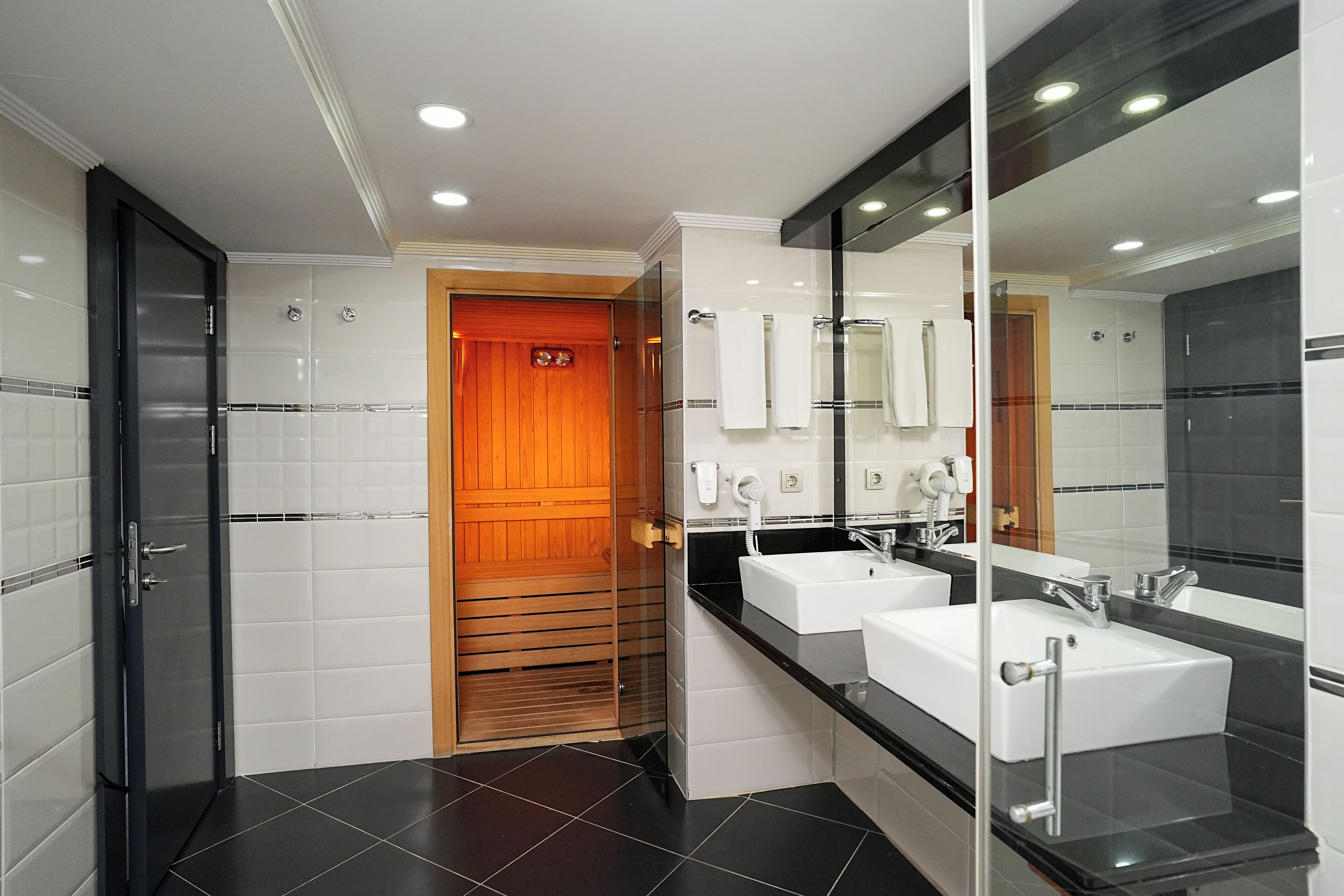 A modern bathroom with two sinks, a glass shower enclosure, and a wooden door.