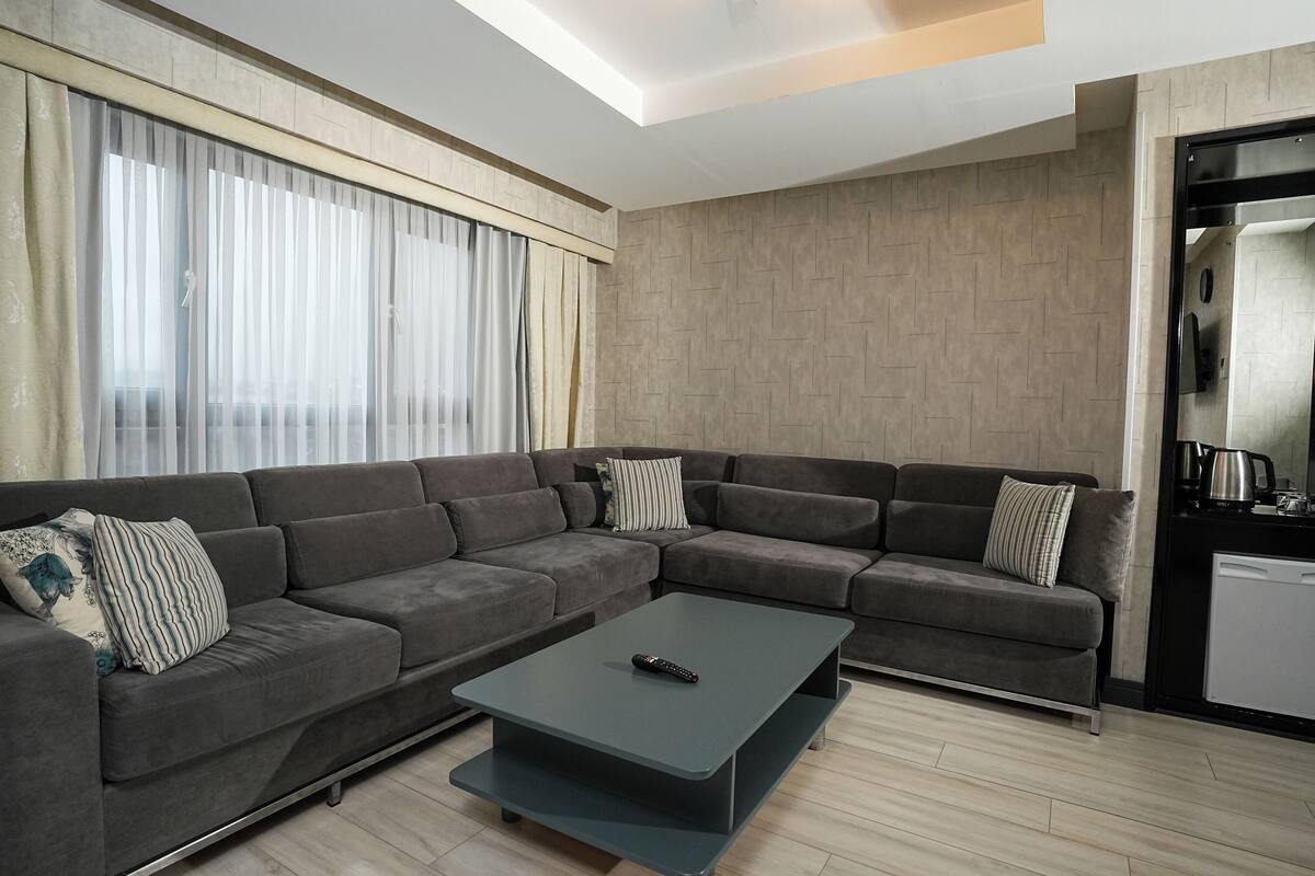 A modern living room with a sectional sofa, a coffee table, and a kitchen area with a dishwasher.