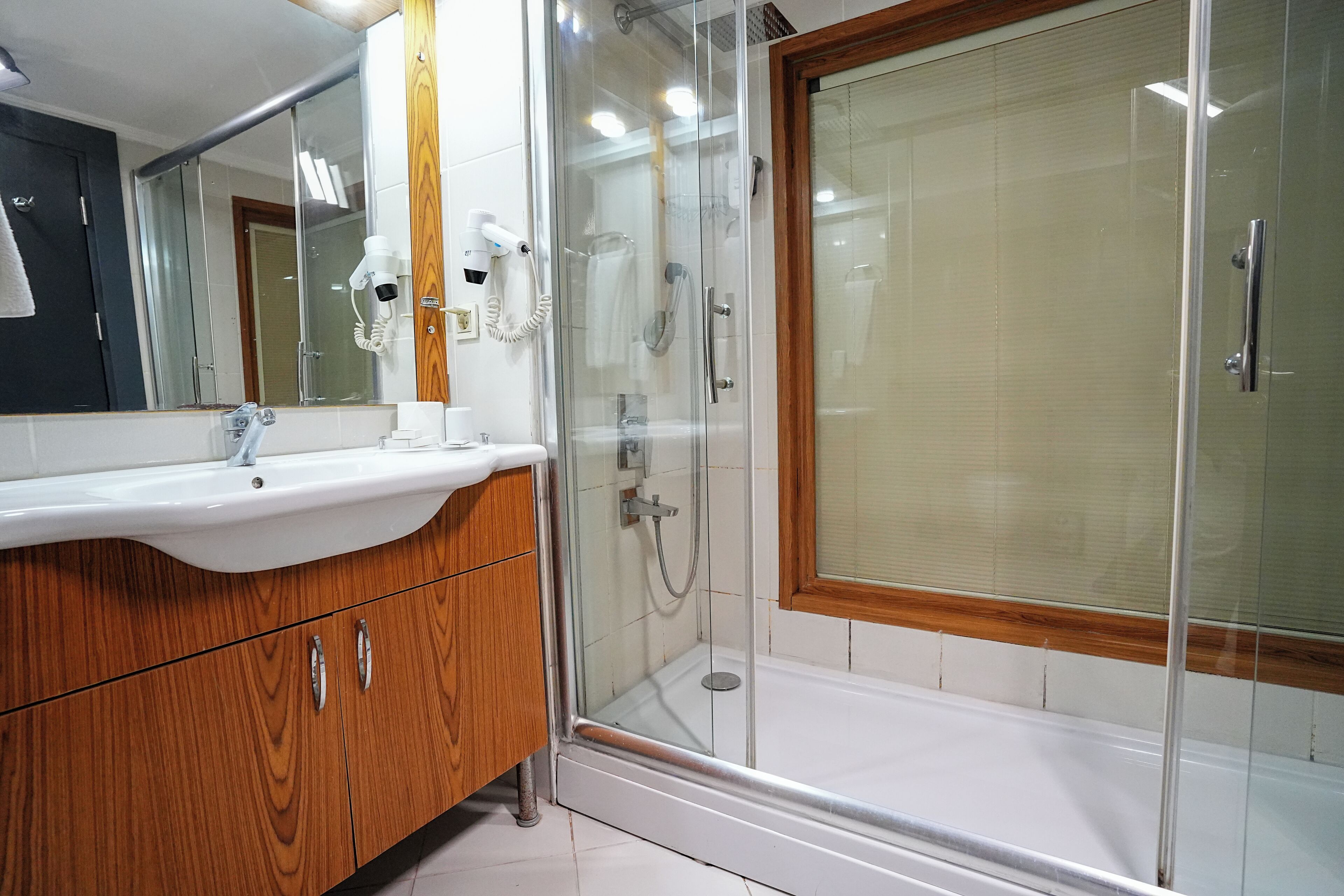 A modern bathroom with a wooden vanity, a glass shower enclosure, and a large mirror.
