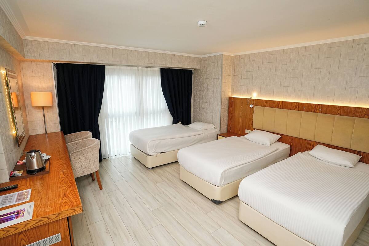 A hotel room with two beds, a wooden desk, a chair, and a window with curtains.