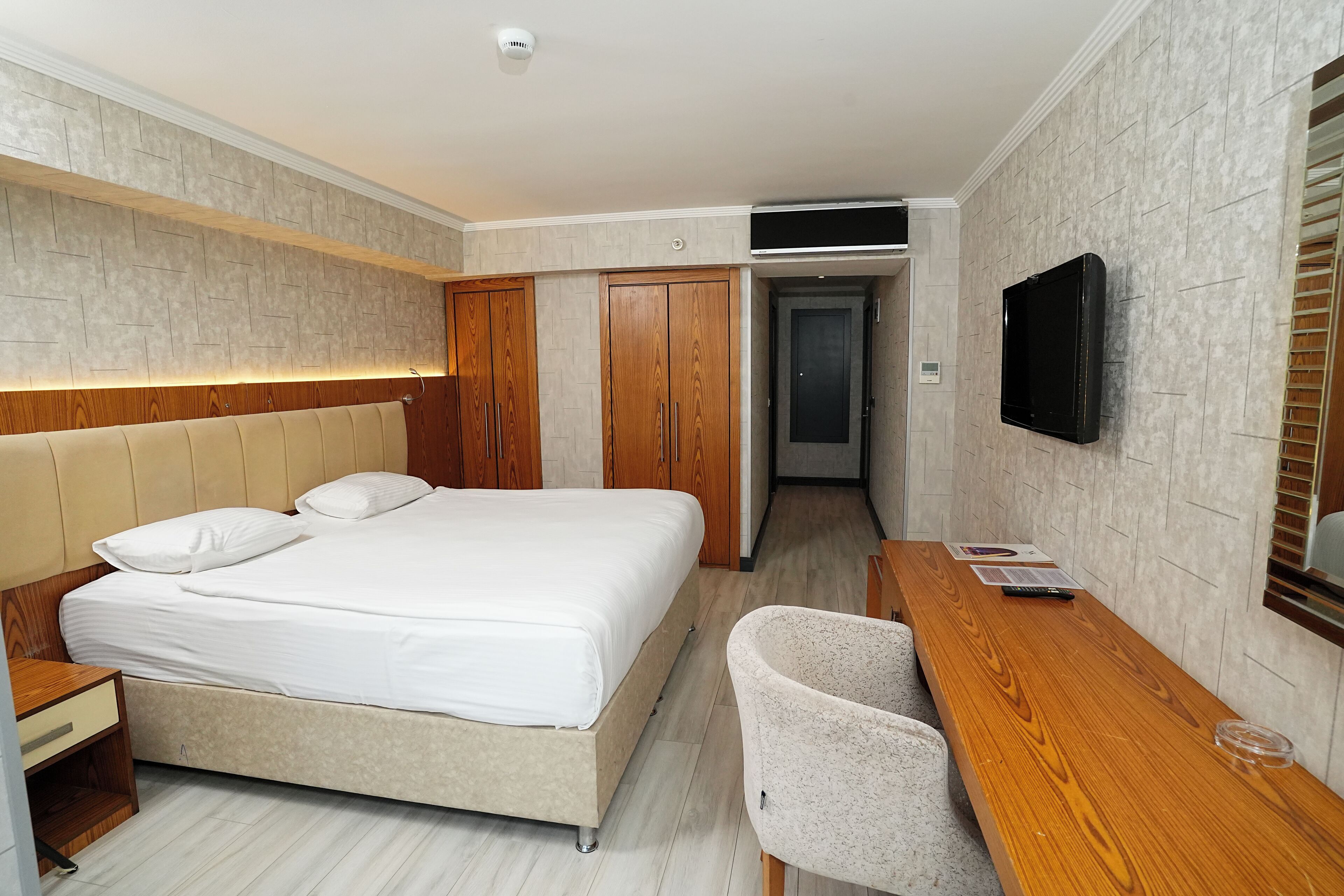A modern hotel room with a bed, wooden wardrobe, a desk, and a TV.