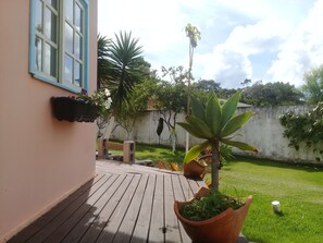A wooden deck with potted plants, a white wall, and a clear sky.