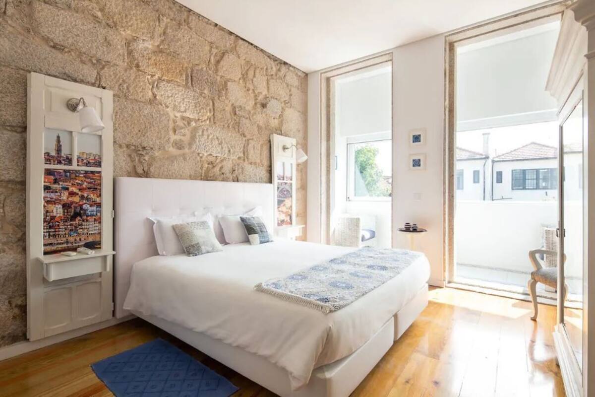 Un dormitorio con pared de piedra, una cama grande, vistas a través de un ventanal y un cartel con un paisaje urbano.