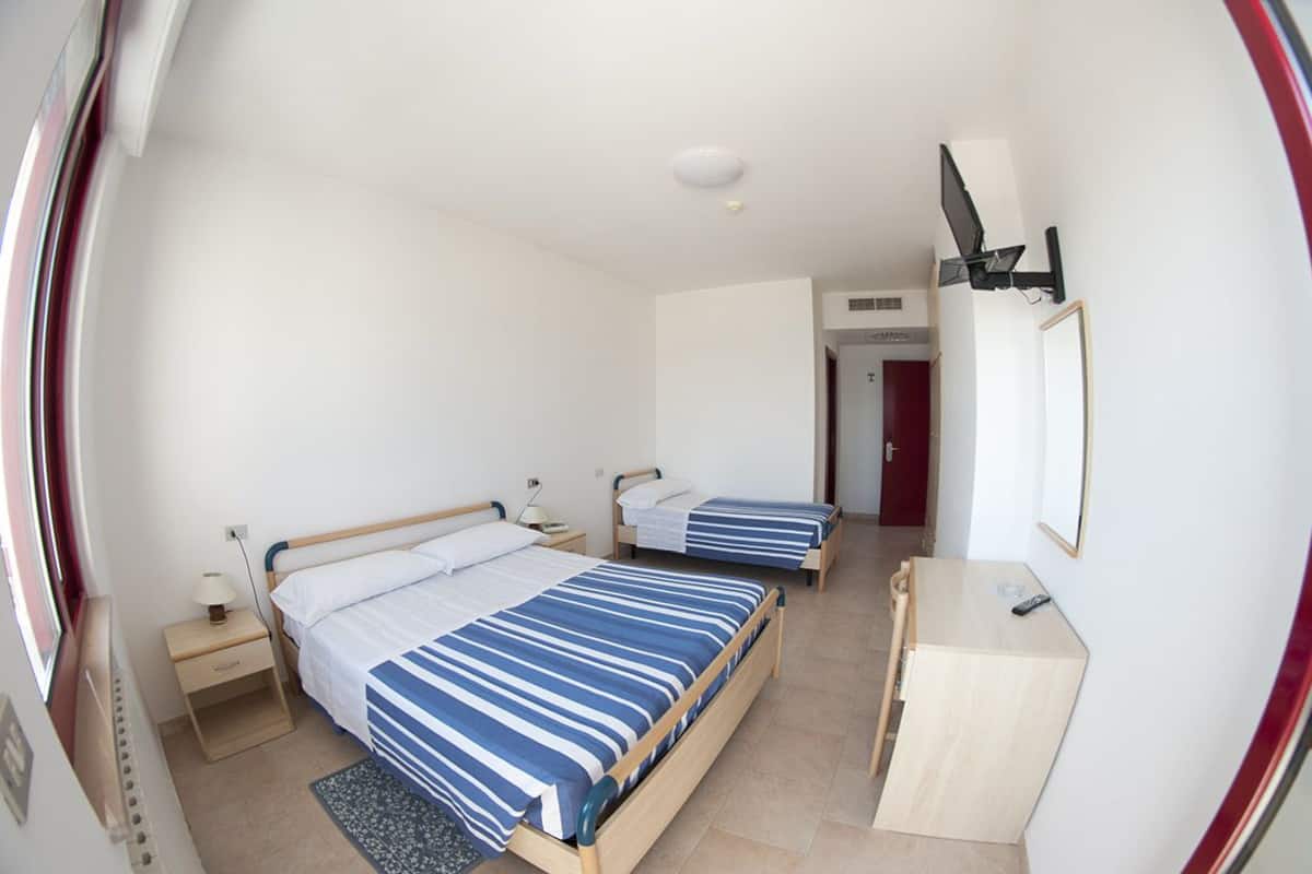 A room with two beds, a desk, a mirror, and a television.