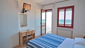 Un dormitorio con cama, escritorio, silla, espejo, ventana y vistas al mar, además de un radiador.