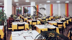 Comedor con varias mesas dispuestas para comidas, con manteles amarillos y sillas negras.