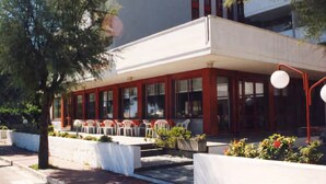 Un hotel con fachada moderna, balcón y mobiliario exterior.