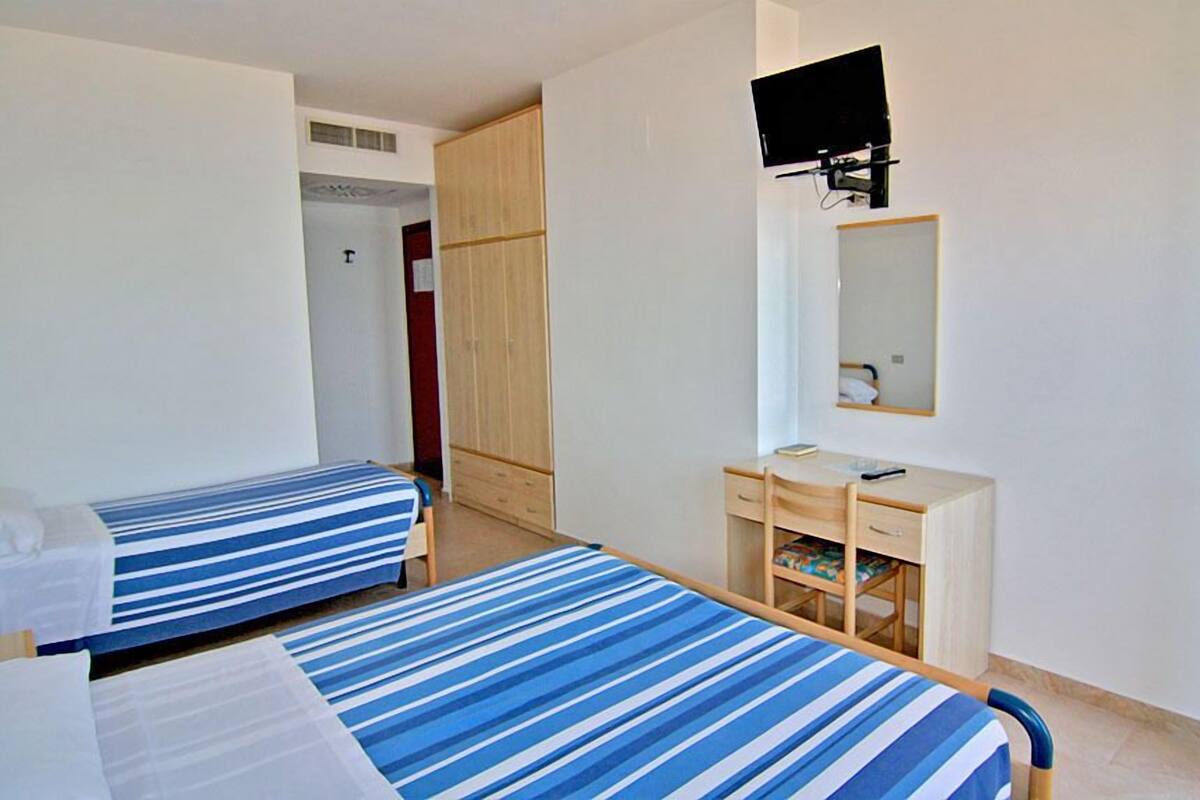 A room with two beds, a desk, a mirror, and a television.