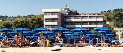 Una playa con hileras de sombrillas azules y sillas reclinables.