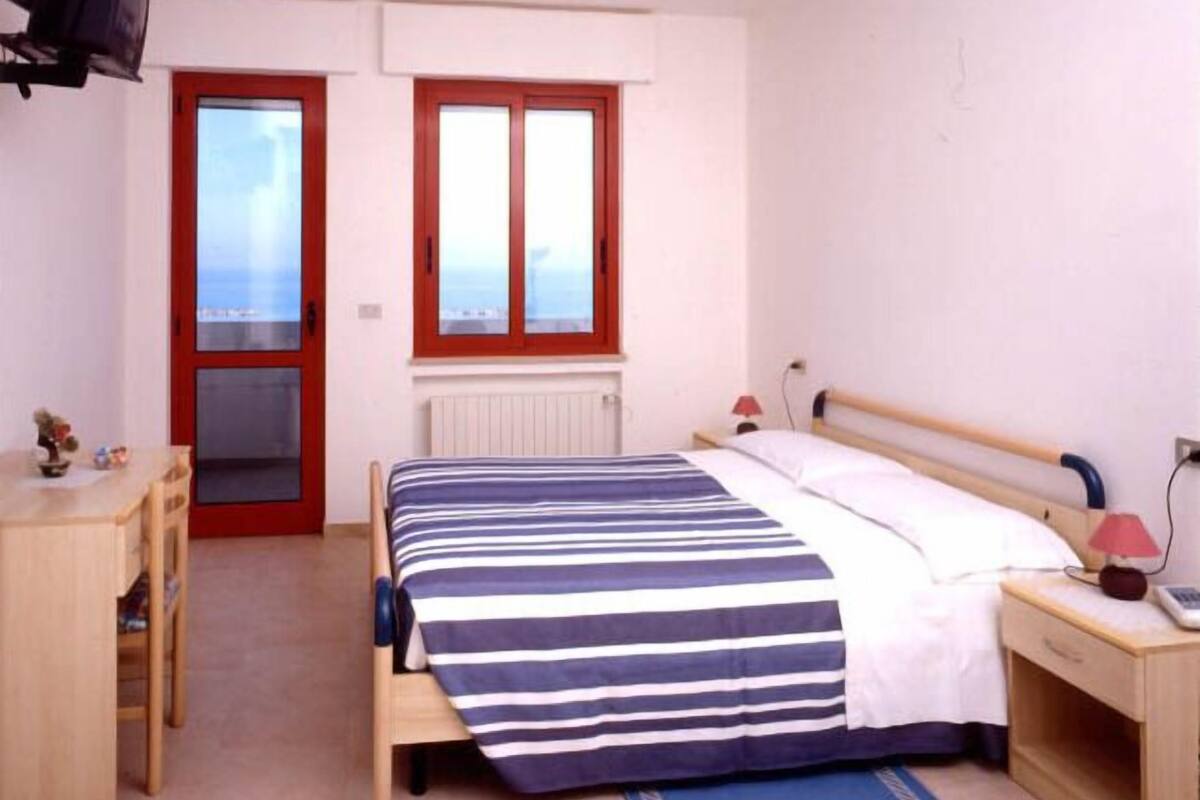 A bedroom with a bed, a desk, a chair, a window, and a radiator.