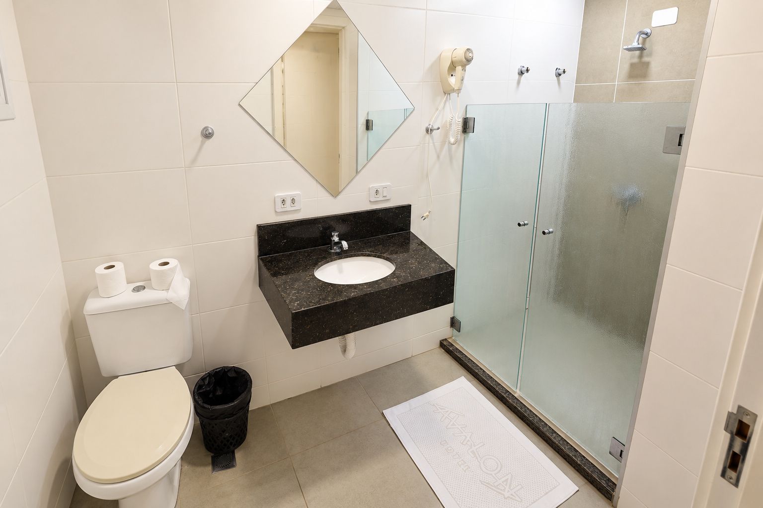 A bathroom with a toilet, sink, mirror, and glass-enclosed shower.