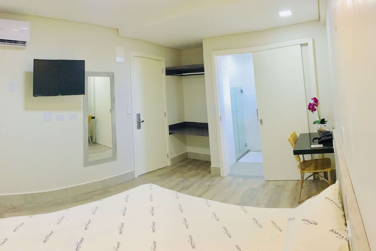 A hotel room with a bed, a TV, a wardrobe, and a desk with a chair.