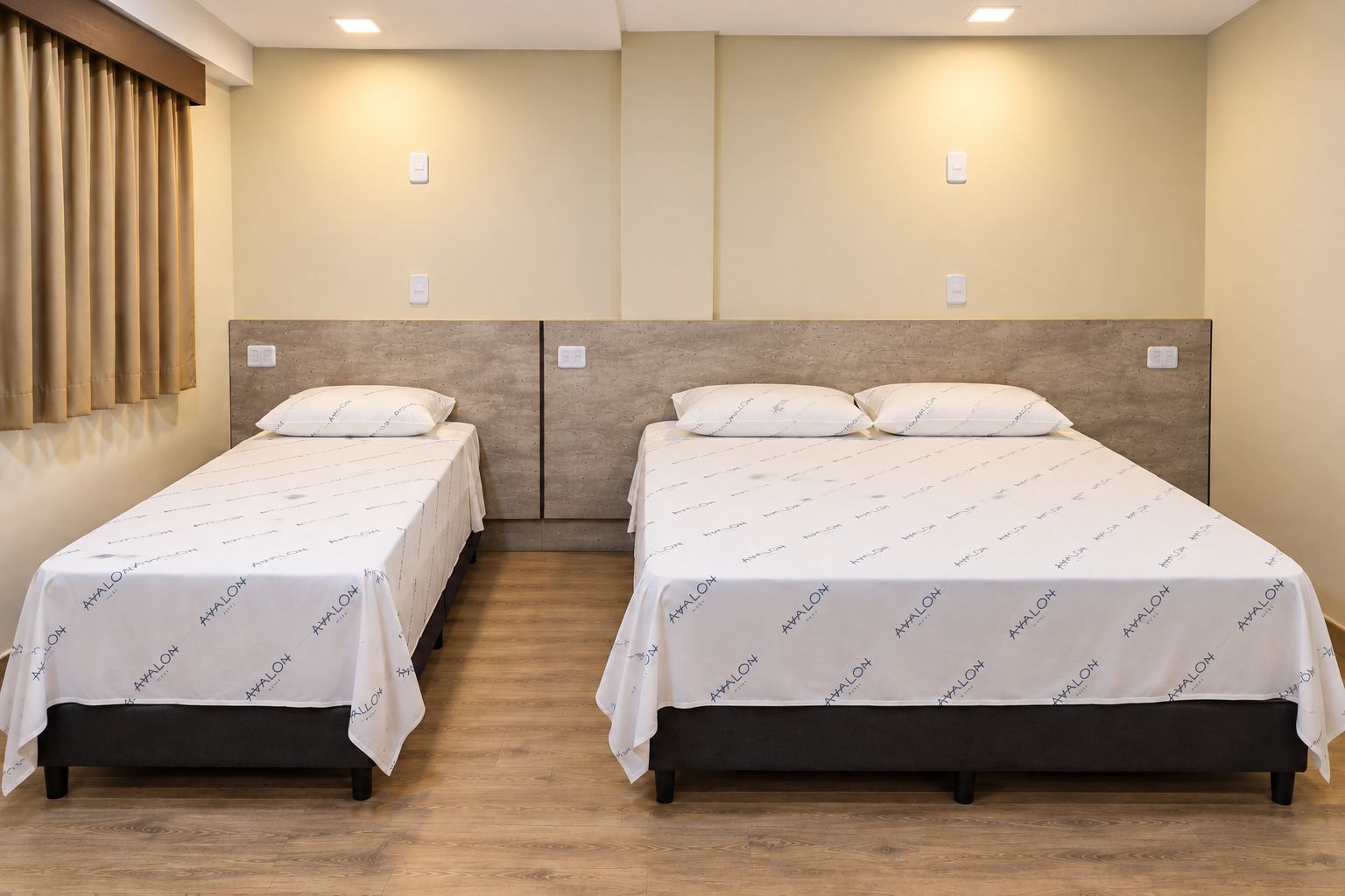A hotel room with two beds, wooden flooring, and a neutral color scheme.