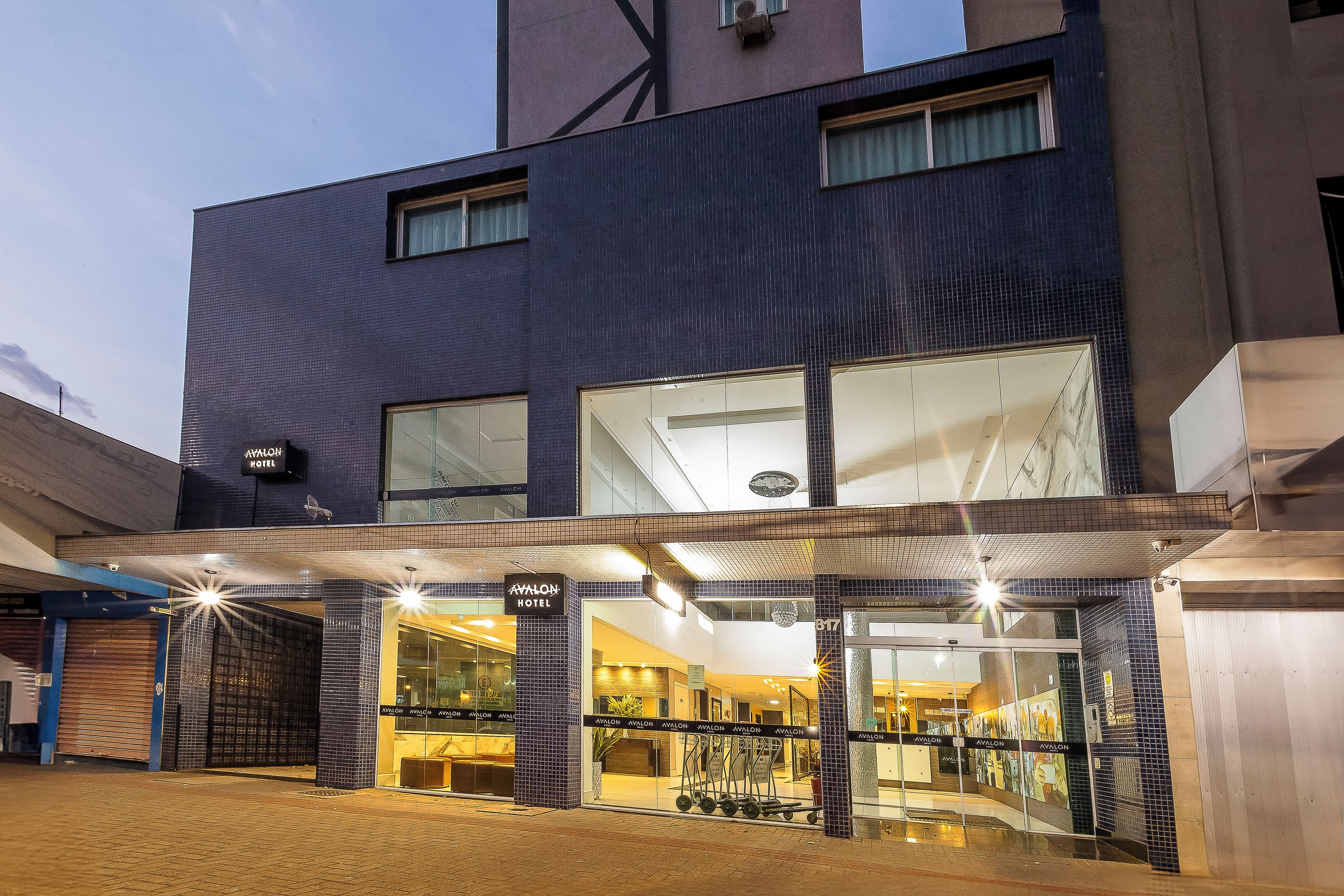 A hotel entrance with a covered outdoor area, a reception desk, and a visible elevator.