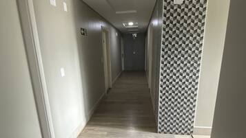 Un pasillo largo y estrecho con un diseño de cuadros en una pared, suelo de madera e iluminación empotrada en el techo.
