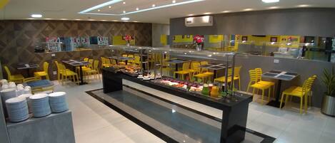 A buffet setup with multiple food stations, yellow chairs, and a modern interior design.