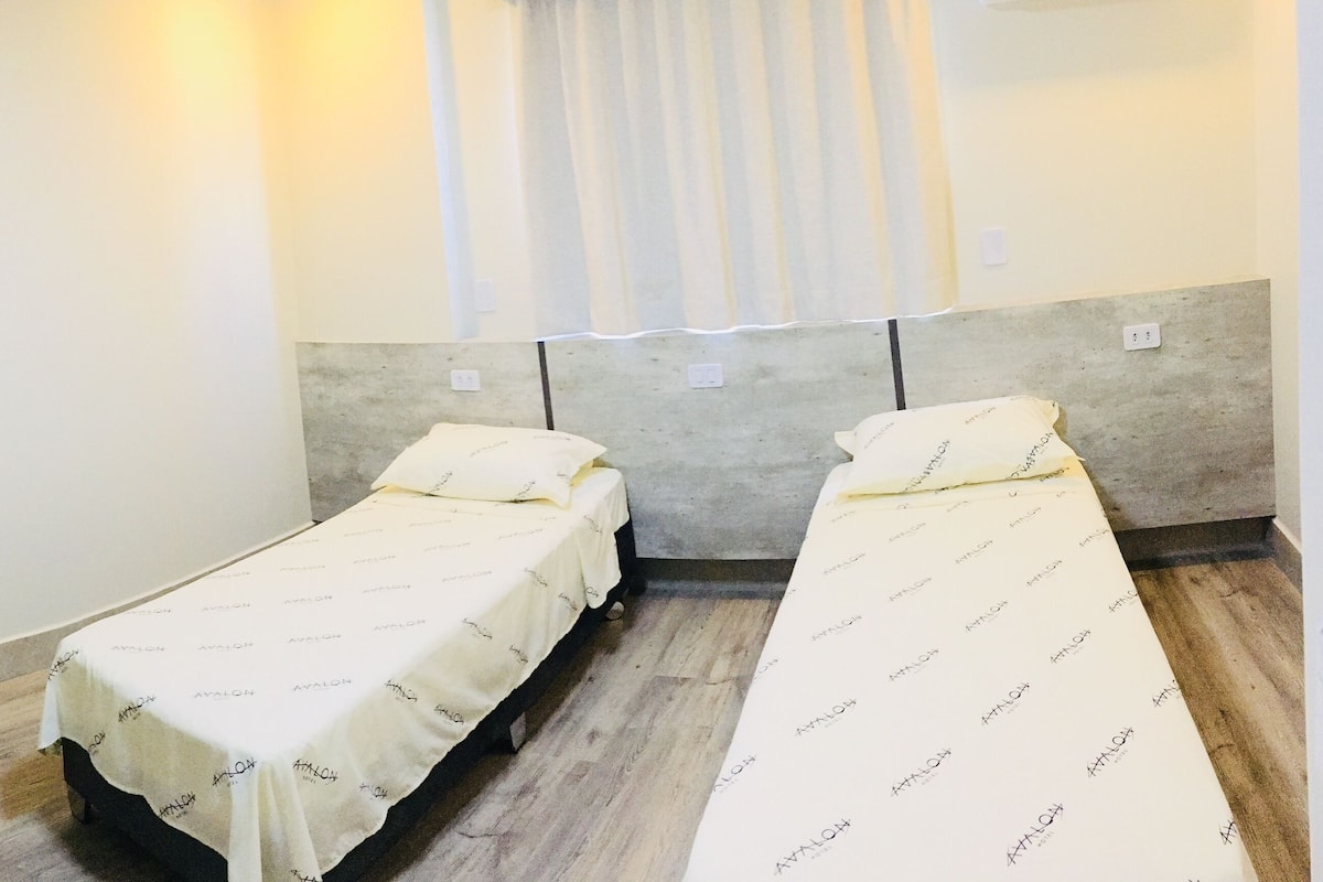 A hotel room with two single beds, a desk with a chair, a TV, and a mirror.