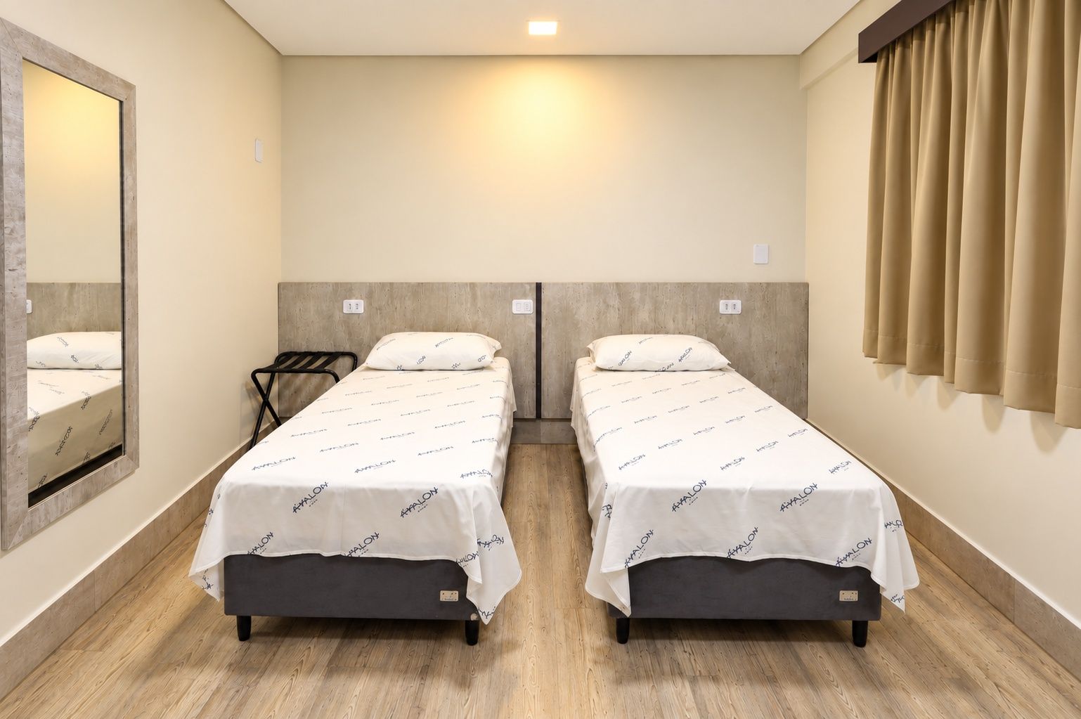 A twin room with two beds, a mirror, and a window with curtains.