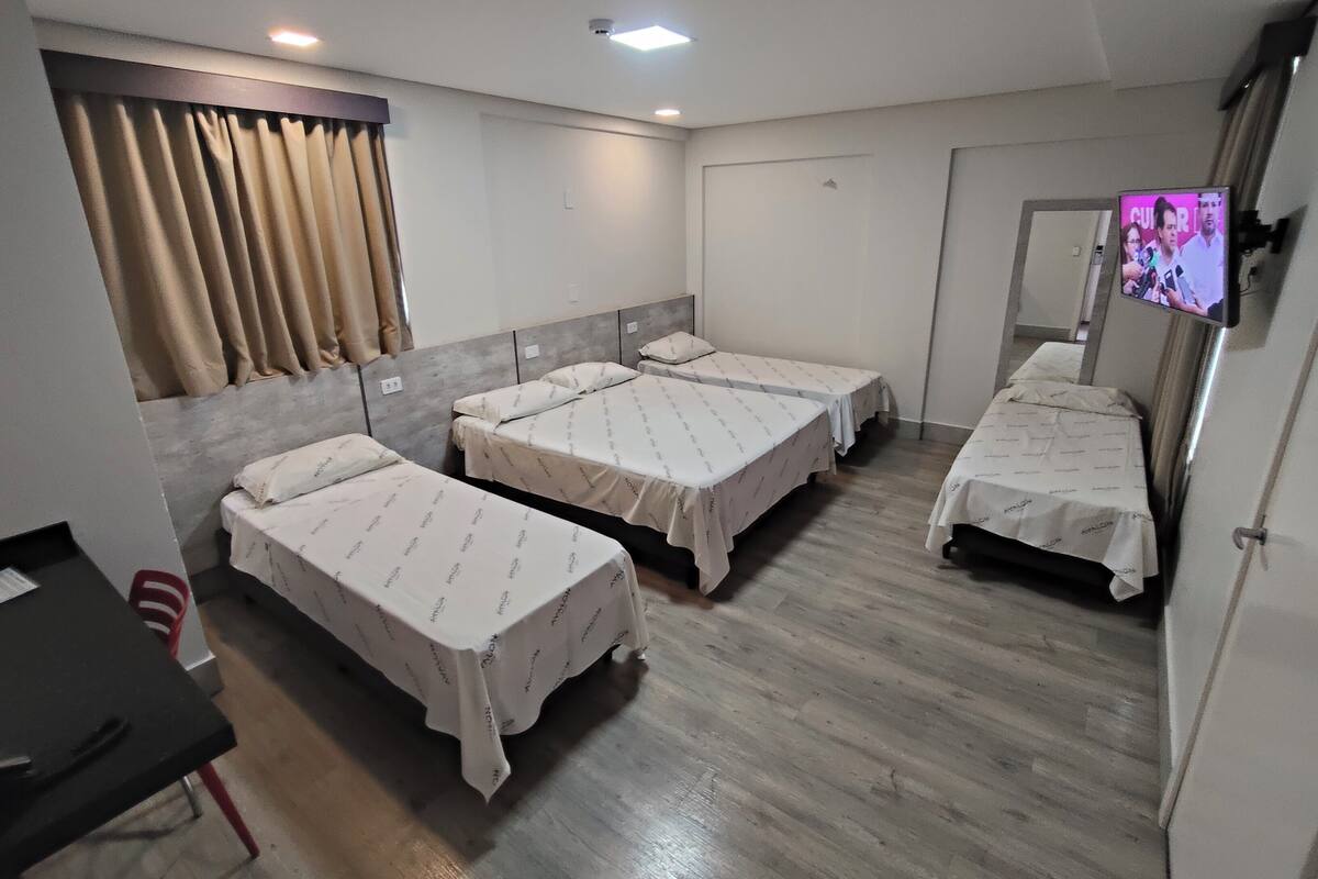 A hotel room with four single beds, a desk, a chair, and a television mounted on the wall.
