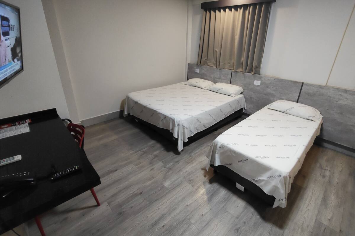 A bedroom with two single beds, a desk, and a television on the wall.