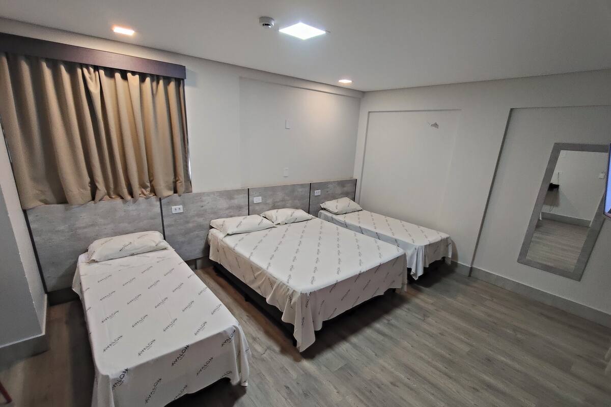 A hotel room with three single beds, a large mirror, and a wooden floor.