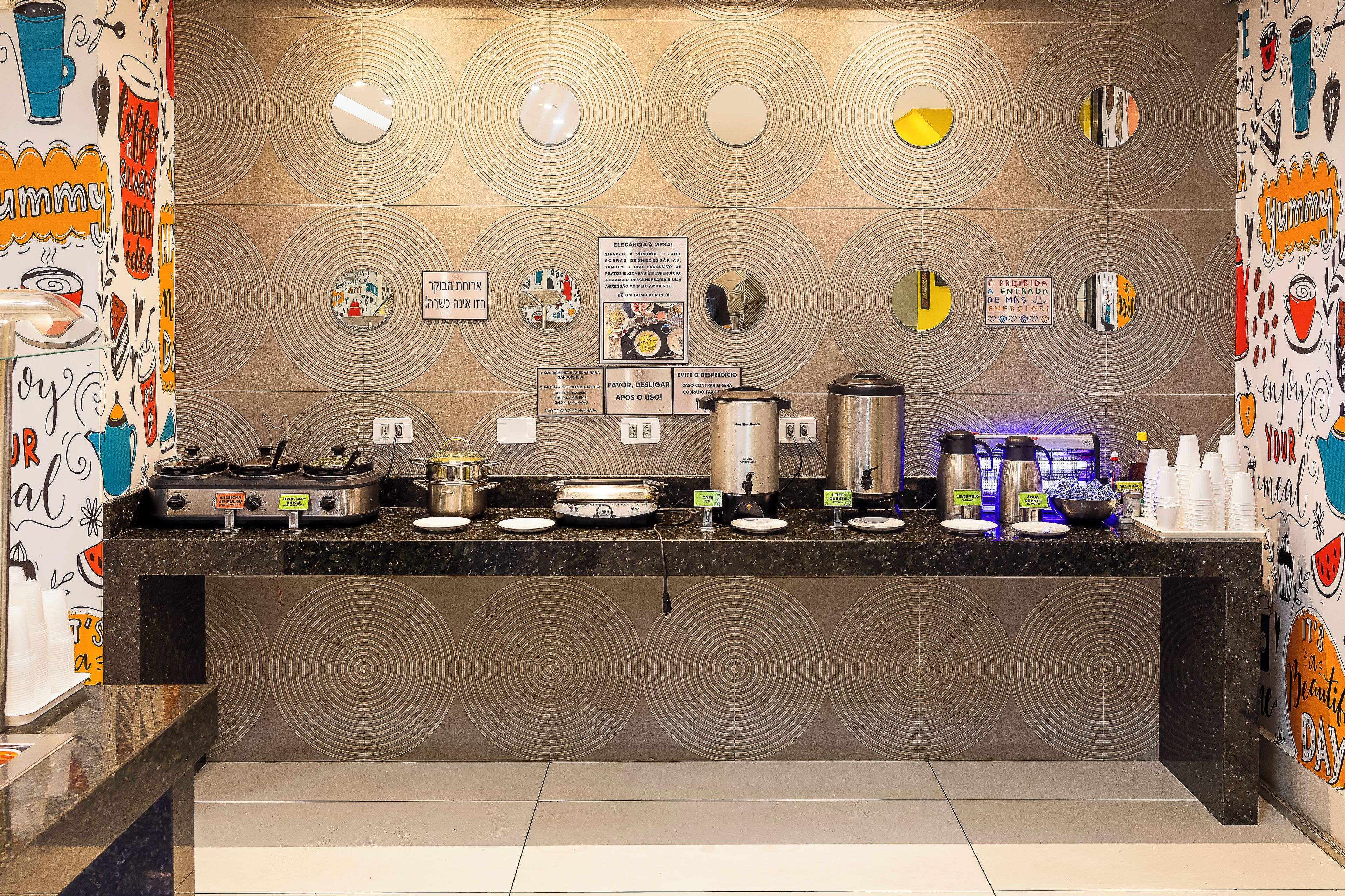Een kitchenette met een behang, diverse apparaten en een koffiehoek.