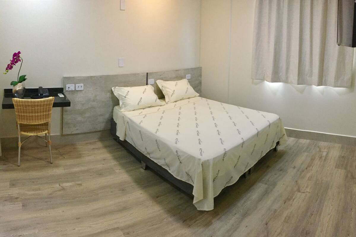 A bedroom with a bed, a chair, a desk, and a vase with flowers.